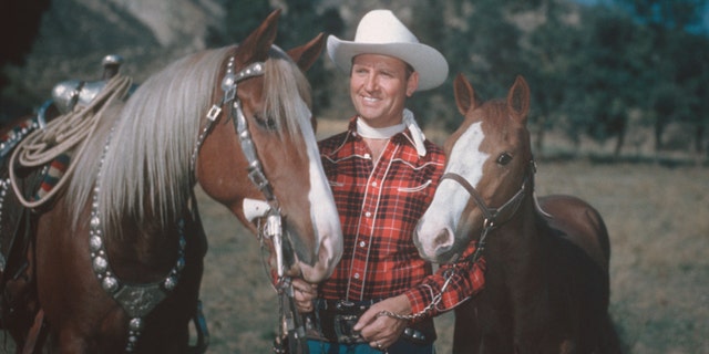 Country and western singer Gene Autry (1907-1998), dressed in cowboy hat and plaid shirt, poses with two horses, circa 1955. Autry gained fame as "The Singing Cowboy" on the radio, in movies and on television. 