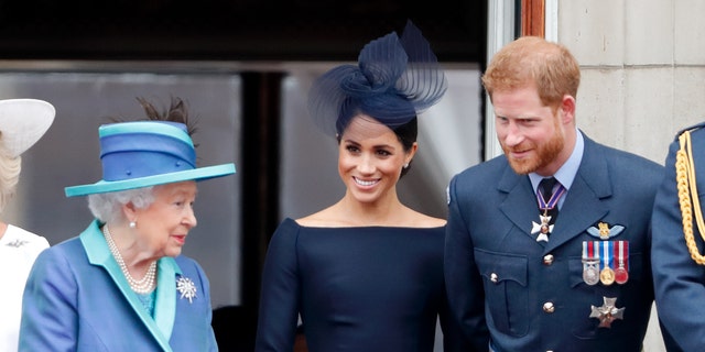 The late Queen Elizabeth II, pictured here with Meghan Markle and Prince Harry in the summer of 2018. Harry's memoir was initially set to be published at the end of 2022.