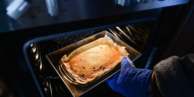A woman takes a homemade cheesecake out of an oven inside her apartment during the coronavirus lockdown on Wednesday, April 1, 2020.