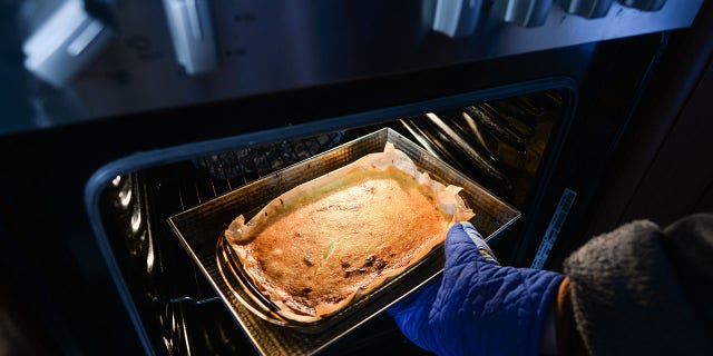 A woman takes a homemade cheesecake out of an oven inside her apartment during the coronavirus lockdown on Wednesday, April 1, 2020.