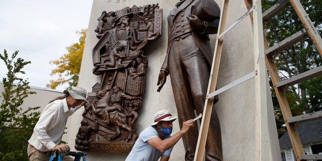 Martin Sylvester, left, buffs a coat of wax he applied to the Uncle Sam Memorial statue in Arlington, Mass., as Mario Marroquin applies wax to the lower half of Uncle Sam's legs on Sept. 28, 2020. The statue commemorates Samuel Wilson, the original Uncle Sam, near his birthplace in Arlington.