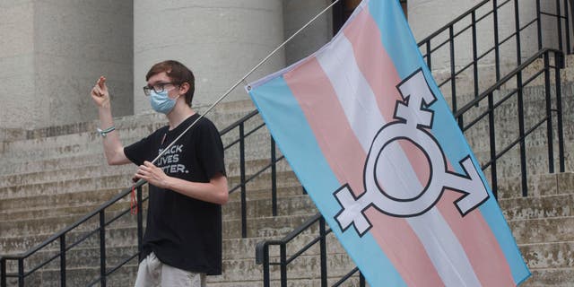 A protester holds the trans flag and snaps in solidarity with other speakers during a demonstration at the Ohio Statehouse in Columbus, Ohio, June 25, 2021.