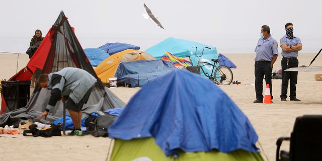Workers with Los Angeles County Beaches and Harbors City keep an eye out homeless pack up their encampments on the beach in Venice on July 30, 2021. 