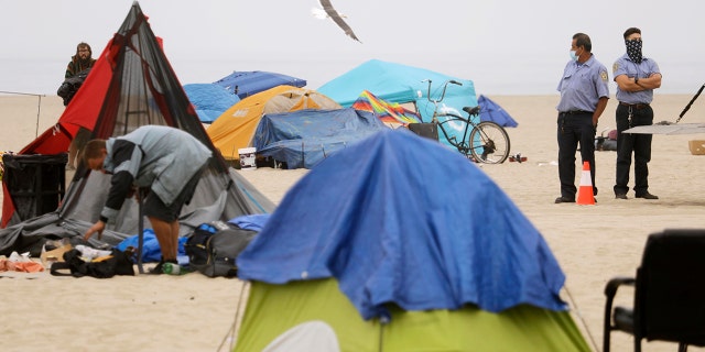 Workers with Los Angeles County Beaches and Harbors City keep an eye out homeless pack up their encampments on the beach in Venice on July 30, 2021. 