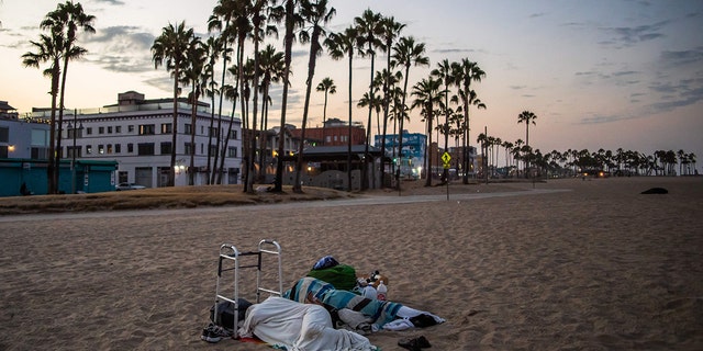 Two homeless people sleep on Venice Beach, California, on August 12, 2021. 