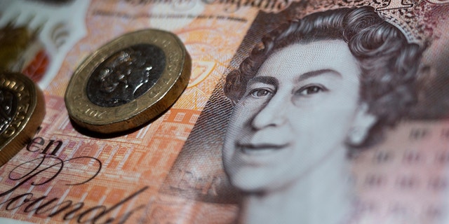 The British currency in the form of two one pound coins rests on a ten pound banknote from the Bank of England with the image of Queen Elizabeth II.