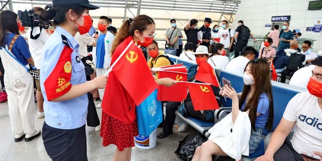 Staff members distribute flags of the Communist Party of China to passengers at Nantong railway station in China's eastern Jiangsu province on June 30, 2022, ahead of the party's 101th anniversary on July 1.