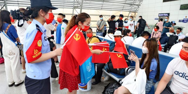 Staff members distribute flags of the Communist Party of China to passengers at Nantong railway station in China's eastern Jiangsu province on June 30, 2022, ahead of the party's 101th anniversary on July 1.