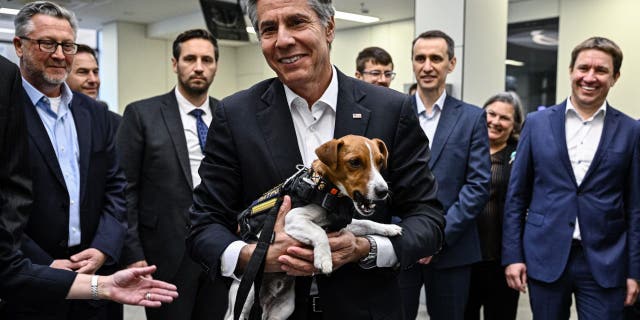 U.S. Secretary of State Antony Blinken (C) holds landmine sniffer dog, a Jack Russell Terrier named Patron during his visit at a children's hospital in Kyiv on September 8, 2022. - Secretary of State Antony Blinken on August 8, 2022, made a surprise trip to Kyiv as the United States unveiled nearly $2.7 billion in new military support to Ukraine and its neighbors to face Russia.
