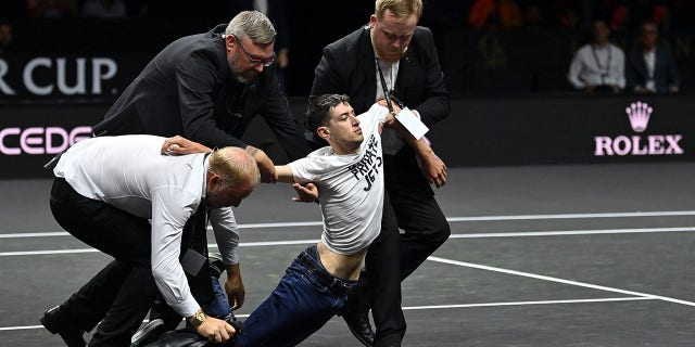 A protester is led away wearing a sign after breaking into the courtroom "end of UK private jets" Stefanos Tsitsipas of Greece's Euro team and Diego Schwarzman of Argentina's World Team during the Laver Cup 2022 at the O2 Arena in London on September 23, 2022. singles match.