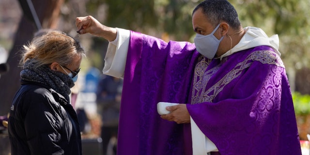 Father Michael Amabisco (right) scatters ashes on a person's head during an Ash Wednesday service at St. Raymond Catholic Church in Menlo Park, California, Wednesday, February 17, 2021.