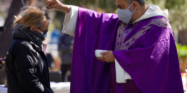 Father Michael Amabisco (right) scatters ashes on a person's head during an Ash Wednesday service at St. Raymond Catholic Church in Menlo Park, California, Wednesday, February 17, 2021.