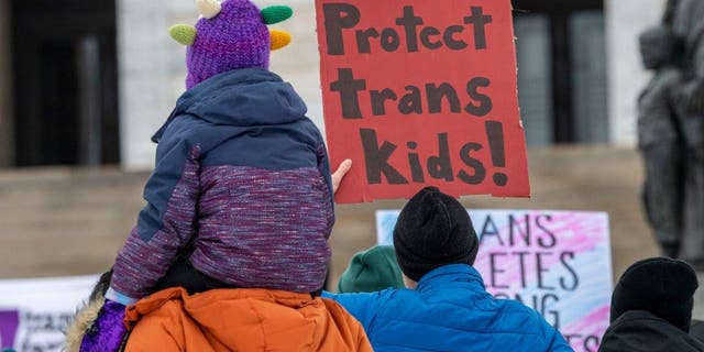 A protester holds a "protect trans kids" sign.