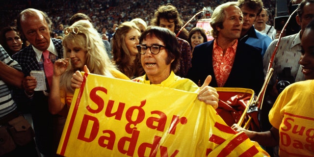 Tennis player Bobby Riggs holds a "Sugar Daddy" sign while being carried to the court by young women. He was about to play a tennis match against Billie Jean King called the "Battle of the Sexes," on Sept. 20, 1973, at the Houston Astrodome. 