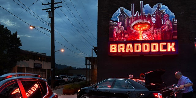 A large art piece featuring neon to simulate a steel pour glows on the side of the old Superior Motors Building in Braddock, Pennsylvania.