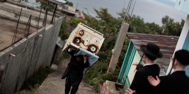 A man from the Lev Tahor, a group of ultra-orthodox Jews, carrying a stove near family members in in the village of San Juan La Laguna in Guatemala, August 28, 2014.