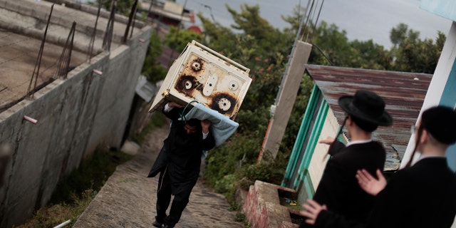 A man from the Lev Tahor, a group of ultra-orthodox Jews, carrying a stove near family members in in the village of San Juan La Laguna in Guatemala, August 28, 2014.