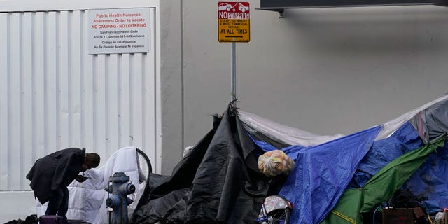 FILE - A man stands near tents on a sidewalk in San Francisco, Nov. 21, 2020. Advocates for homeless people sued the city of San Francisco, Tuesday, Sept. 27, 2022, demanding that it stop harassing and destroying belongings of people living on the streets and commit to spending $4 billion for affordable housing. (AP Photo/Jeff Chiu, File)