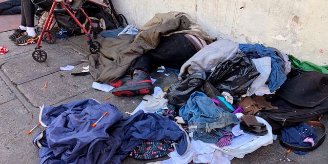 FILE - People sleep near discarded clothing and used needles on a street in the Tenderloin neighborhood in San Francisco, on July 25, 2019. Advocates for homeless people sued the city of San Francisco, Tuesday, Sept. 27, 2022, demanding that it stop harassing and destroying belongings of people living on the streets and commit to spending  billion for affordable housing. (AP Photo/Janie Har, File)