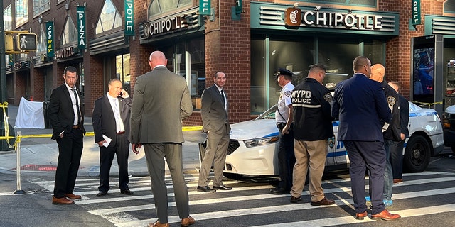 NYPD detectives stand outside a Chipotle near where a 25-year-old woman was fatally shot. 