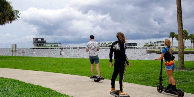 People ride along the bayfront as an outer band of Hurricane Ian approaches and kicks up the surf at Vinoy Park, Tuesday, Sept. 27, 2022, in St. Petersburg, Florida.