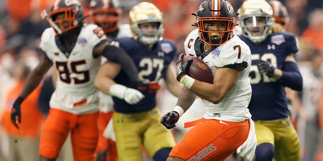 #7 of the Oklahoma State Cowboys, trailing Jaylen Warren, conducts a football against the Notre Dame Fighting Irish during the PlayStation Fiesta Bowl at State Farm Stadium on January 1, 2022 in Glendale, Arizona.