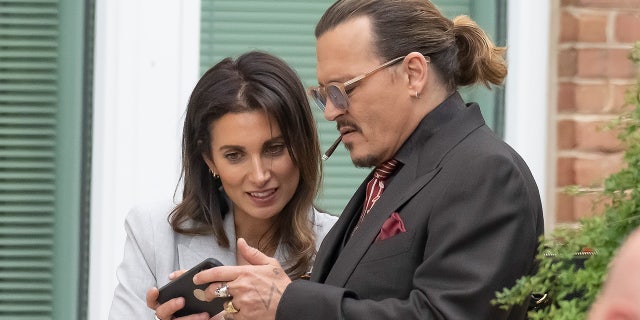 actor Johnny Depp smokes a cigarette as he shows his girlfriend, Joelle Rich, something on his phone.