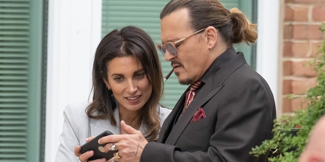 Johnny Depp smokes a cigarette as he shows his girlfriend, Joelle Rich, something on his phone.