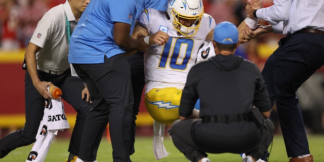 Justin Herbert, #10 of the Los Angeles Chargers, is helped off the field by the medical staff after being hit during the fourth quarter against the Kansas City Chiefs at Arrowhead Stadium on September 15, 2022, in Kansas City, Missouri.
