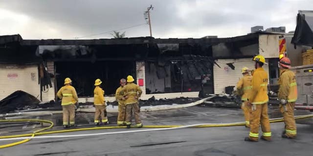 Los Angeles firefighters stand outside a burned up strip mall in the Palms area of LA.