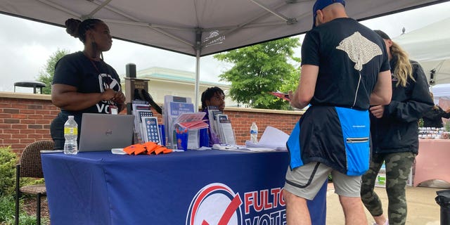 People visit a booth set up by Fulton County to recruit new poll workers at the Alpharetta Farmers Market on Sept. 10, 2022, in Alpharetta, Ga. Lies about the integrity of the 2020 presidential contest by former President Donald Trump and his allies are spurring new interest in working the polls in Georgia and elsewhere in the nation for the upcoming midterm elections. (AP Photo/Sudhin Thanawala)