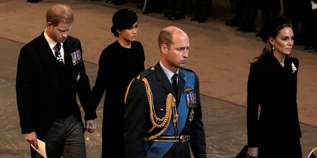 Prince William and Kate Middleton lead procession as Queen Elizabeth II's coffin is transported to Westminster Hall, with Prince Harry and Meghan Markle standing in the distance.