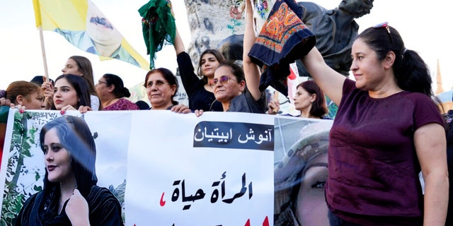 Kurdish women activists hold headscarves and a portrait of Iranian woman Mahsa Amini, with Arabic that reads, 