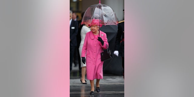 Queen Elizabeth II takes shelter under an umbrella as she visits the newly refurbished Birmingham New Street Station on November 19, 2015, in Birmingham, England.