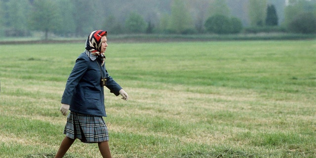 The Queen in laced up brogue shoes and raincoat walking In Windsor Great Park in the grounds of Windsor Castle. 