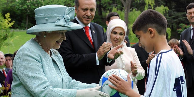 Britain's Queen Elizabeth II presents a football to a child while Turkish Prime Minister Recep Tayyip Erdogan and his wife Emine Erdogan watch the British Embassy in Ankara on May 16, 2008.