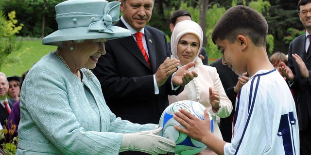 Britain's Queen Elizabeth II hands a football to a child as Turkish Prime Minister Tayyip Erdogan and his wife Emine Erdogan look on at the British Embassy in Ankara on May 16, 2008.