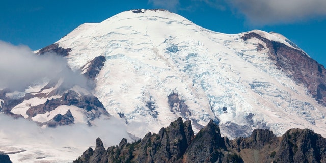 Mount Rainier, a stratovolcano, covered by ice of the Emmons Glacier. Mount Rainier National Park, Washington. Cowlitz Chimneys in foreground. 