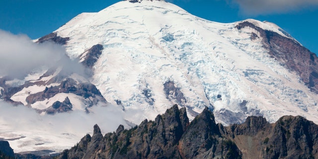 Mount Rainier, a stratovolcano, covered by ice of the Emmons Glacier. Mount Rainier National Park, Washington. Cowlitz Chimneys in foreground.