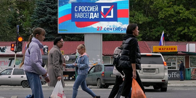 People walk past a billboard reading "Forever with Russia" in Luhansk, Luhansk People's Republic controlled by Russia-backed separatists, eastern Ukraine, Tuesday, Sept. 27, 2022. 