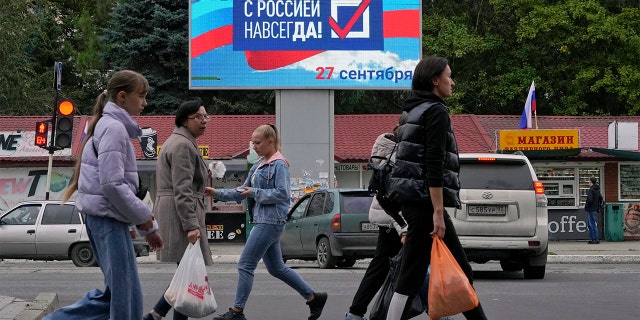 People pass a billboard "Forever with Russia" in Luhansk, Luhansk People's Republic controlled by Russian-backed separatists, eastern Ukraine, Tuesday, September 27, 2022. 