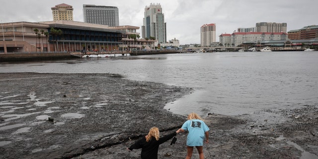 Sisters Angel Disbrow (R) and Selena Disbrow walk along the shore of a receded Tampa Bay as water was pulled out from the bay in advance of the arrival of Hurricane Ian on Sept. 28, 2022, in Tampa, Florida. 