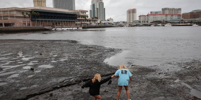 Sisters Angel Disbrow (R) and Selena Disbrow walk along the shore of a receded Tampa Bay as water was pulled out from the bay in advance of the arrival of Hurricane Ian on Sept. 28, 2022, in Tampa, Florida.