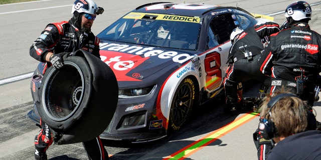 A crew member for Tyler Reddick's No. 8 car, left, carries a damaged tire away during a pit stop at a NASCAR Cup Series auto race at Kansas Speedway in Kansas City, Kan., Sunday, Sept. 11, 2022.