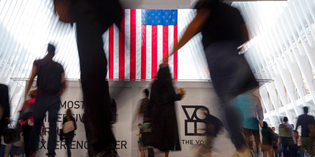 FILE: People walk past an American flag at the start of a work day, at the Oculus, part of the World Trade Center transportation hub in New York, Sept. 11, 2019.