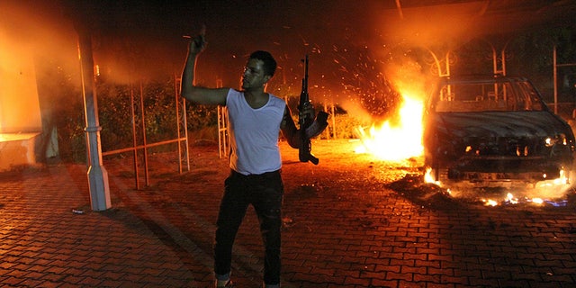 A man waves his rifle as buildings and cars are engulfed in flames inside the U.S. consulate compound in Benghazi late on Sept. 11, 2012. Four Americans were killed in the attack, which also targeted a CIA annex about a mile away from the consulate. 