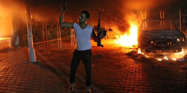 A man waves his rifle as buildings and cars are engulfed in flames inside the U.S. consulate compound in Benghazi late on Sept. 11, 2012. Four Americans were killed in the attack, which also targeted a CIA annex about a mile away from the consulate.