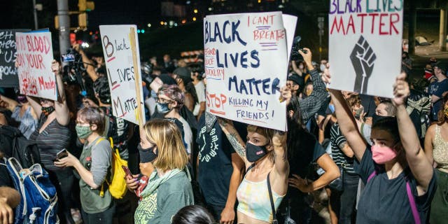 People hold up signs outside Austin Police Department after a vigil for Garrett Foster on July 26, 2020 in downtown Austin, Texas.