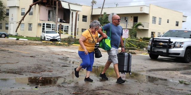 King Point resident Maria Esturilho is escorted by her son, Tony Esturilho, as they leave behind the damage from an apparent overnight tornado spawned from Hurricane Ian at Kings Point 55+ community in Delray Beach, Fla., on Wednesday, Sept. 28, 2022.  