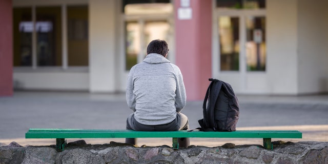 A young man sits on a bench next to his backpack at school. There has been a "big change" in the way schools approach mental health issues today, said MacPhee of The Jed Foundation.